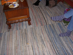 Picture of the floor which has an old rag rug which is sewn together in sections and has a hole in it.