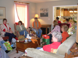 People sitting around smiling with presents sitting on floor and tables.